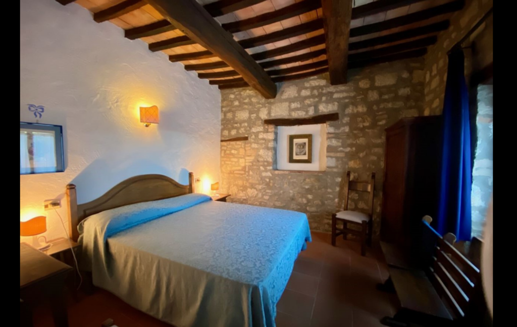 Bedroom with stone wall and blue bedspread in the Dolce Fede apartment